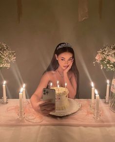 a woman sitting in front of a cake with candles on it and looking at her cell phone