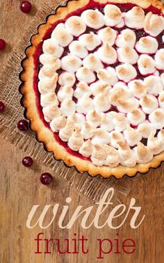 a pie topped with fruit and marshmallows sitting on top of a wooden table