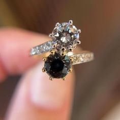 a close up of a person's hand holding an engagement ring with two diamonds on it