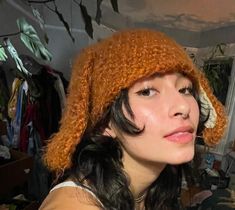 a woman wearing a knitted orange hat in a room with clothes on the walls