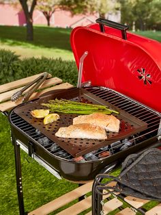 a red grill with chicken and asparagus on it in front of a picnic table