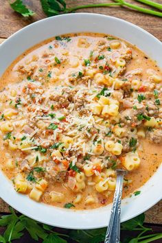 a white bowl filled with pasta and meat soup on top of a wooden table next to parsley