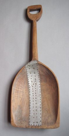 an old wooden spatula with metal strips on the handle and sides, hanging from a wall