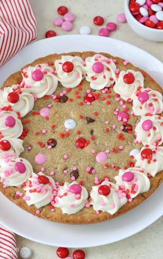 a cookie cake with white frosting and sprinkles on a plate next to candy