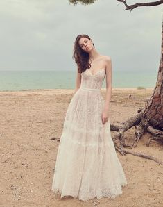 a woman standing on top of a sandy beach next to a tree and the ocean