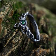 a silver ring with green stones on top of a mossy tree branch in the woods