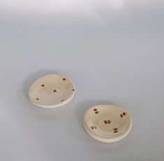 two white bowls with red flowers on them sitting side by side against a gray background