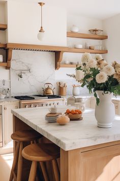 a kitchen with marble counter tops and wooden stools next to a white vase filled with flowers