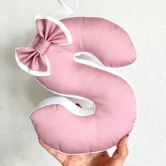 a person holding up a pink and white pillow with a bow on the letter s