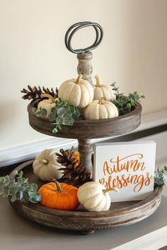 two tiered trays with pumpkins and greenery on the top one has a sign that says autumn belongs