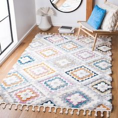 a white rug with multicolored diamonds and tassels on the floor in front of a mirror