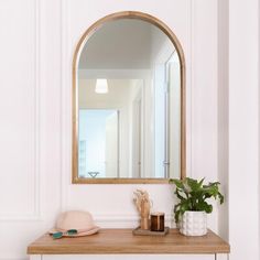 a mirror on the wall above a wooden table with a hat and potted plant