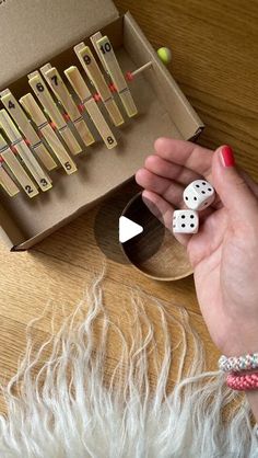 a person holding two dices in front of a box full of dominoes on a table