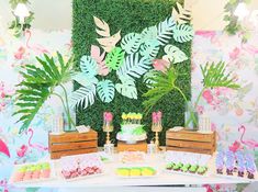 a table topped with cakes and desserts next to a wall covered in greenery