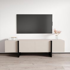 a tv mounted to the side of a white wall next to a vase with flowers