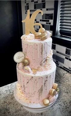 a pink cake with gold decorations and the number six on top is sitting on a counter