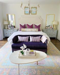 a bedroom with a large bed, purple couch and coffee table in front of it