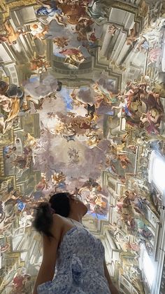 a woman sitting on the ground in front of a ceiling with many paintings all over it