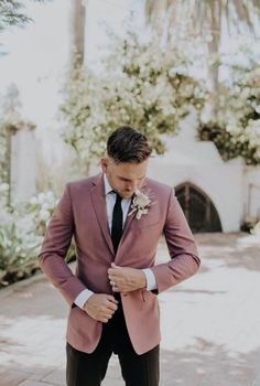 a man in a suit and tie is looking down at his shirt while standing on the sidewalk