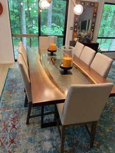 a dining room table with chairs and candles on it in front of a large window