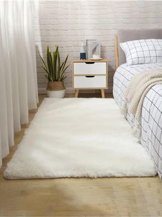 a bedroom with a white rug on the floor next to a bed and nightstand in front of a brick wall