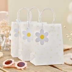 three small bags with flowers on them sitting next to some sunglasses and a pair of pink eyeglasses