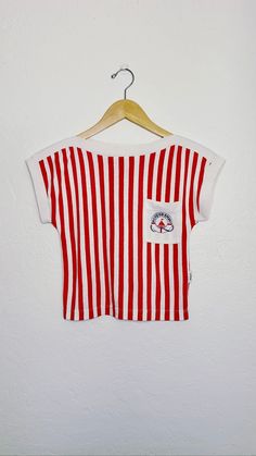 "70s vintage red and white striped crop shirt with capped sleeves and front logo pocket on left breast.  Soft poly cotton blend fabric, high neck, and cap sleeves make this the perfect summer top s i z e small m e a s u r e m e n t s bust: 30\" waist: 28\" length: 16\" sts: 32\" al: 14\" m a t e r i a l poly / cotton blend c o n d i t i o n good vintage; some signs of fading and wear c a r e machine wash delicate hang or tumble dry low" Sporty Striped T-shirt For Summer, Casual Cotton Tops With Vertical Stripes, White T-shirt With Contrast Stripes For Summer, Casual Cotton Tops With Striped Hem, Cotton Tops With Vertical Stripes And Short Sleeves, White Contrast Stripes T-shirt For Summer, Striped T-shirt With Contrast Stripes For Summer, Striped Short Sleeve Summer Top, Summer Striped Short Sleeve Tops