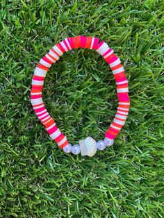 a pink and white beaded bracelet laying on top of green grass with two seashells