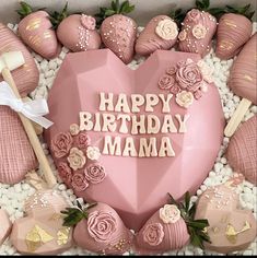 a pink heart shaped cake surrounded by chocolates and flowers with the words happy birthday mama written on it