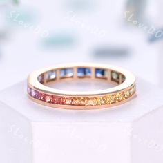 a gold ring with multicolored stones on the inside and outside, sitting on top of a white surface