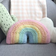 a crocheted rainbow pillow sitting on top of a couch next to a stuffed animal