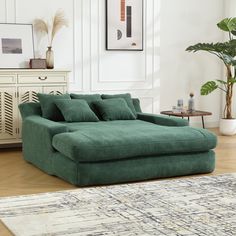 a green couch sitting on top of a wooden floor next to a white dresser and potted plant