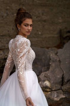 a woman in a white dress is standing near rocks