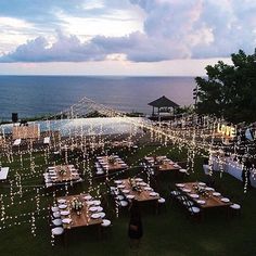 an outdoor dining area overlooking the ocean with lights strung from it and tables set up for dinner