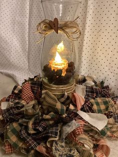 a glass jar with a lit candle in it sitting on top of some plaid fabric