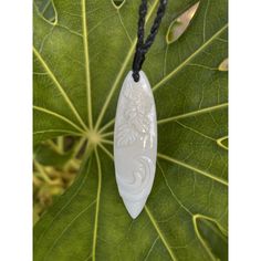 a white jade pendant on a black cord with leaves in the background and green leaves around it