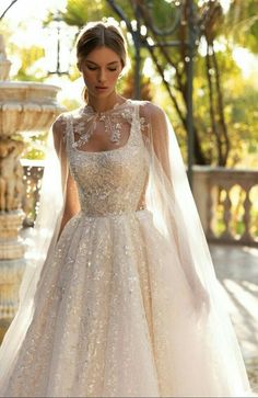 a woman in a wedding dress with a veil on her head is standing near a fountain