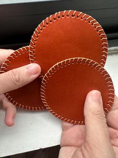 two brown leather discs being held by someone's hands