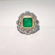 an emerald and diamond ring on a white surface