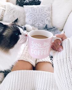 a cat sitting on top of a couch next to a woman holding a coffee cup