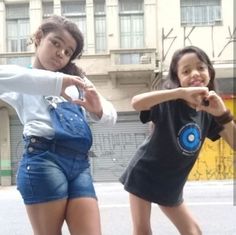 two girls are posing for the camera in front of a building with graffiti on it