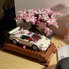 a toy car is parked under a tree with pink flowers on the top and bottom