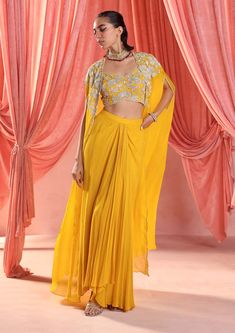 Dazzle in this enchanting ensemble: an embellished choli paired seamlessly with an embellished cape, adding a touch of drama and elegance. Complete the look with a draped skirt for effortless grace and sophistication, perfect for any glamorous affair. Yellow Dhoti Dress For Haldi Function, Yellow Dress For Haldi Function For Sister, Dhoti Skirt Outfits With Cape, Festive Party Wear Sets With Draped Sleeves, Party Wear Sets With Draped Sleeves For Reception, Festive Georgette Cape Sets, Designer Pre-draped Saree With Cape Sleeves For Eid, Georgette Cape Sets, Festive Dress With Sheer Dupatta And Cape