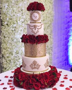 a three tiered wedding cake with red roses on the bottom and gold trimmings