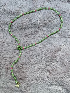 a green and pink beaded necklace on a gray blanket with a gold cross charm