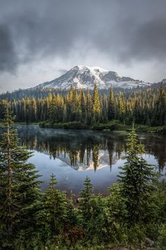 a lake surrounded by trees with a snow capped mountain in the backgrounnd