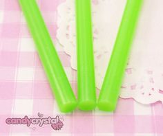 three green plastic straws sitting on top of a pink and white checkered table cloth