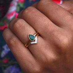 a woman's hand wearing a ring with a pear shaped green stone on it