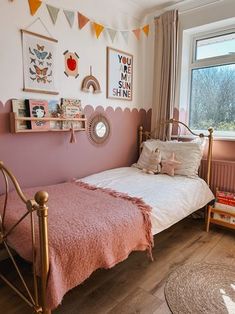 a bedroom with pink walls and wooden flooring, decorated with pictures on the wall