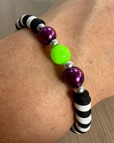 a woman's arm wearing a black and white striped bracelet with green, purple, and silver beads